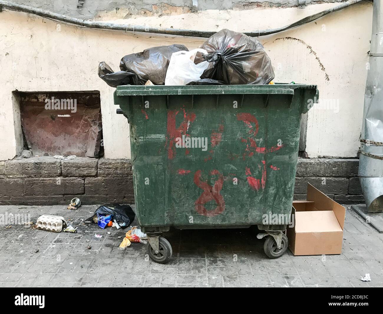 green-dirty-trash-dumpster-front-view-next-to-the-wall-of-the-old-building-opened-city-trash-c...jpg